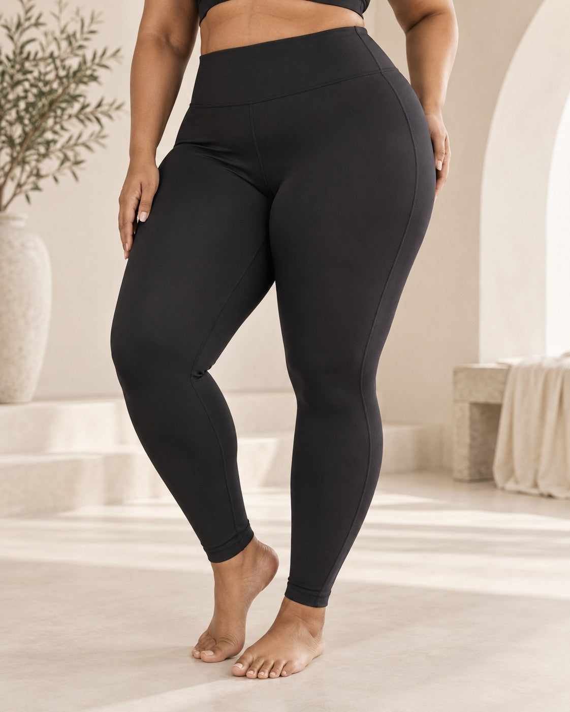 Woman wearing ROMY plus-size leggings in a sunlit stone studio
